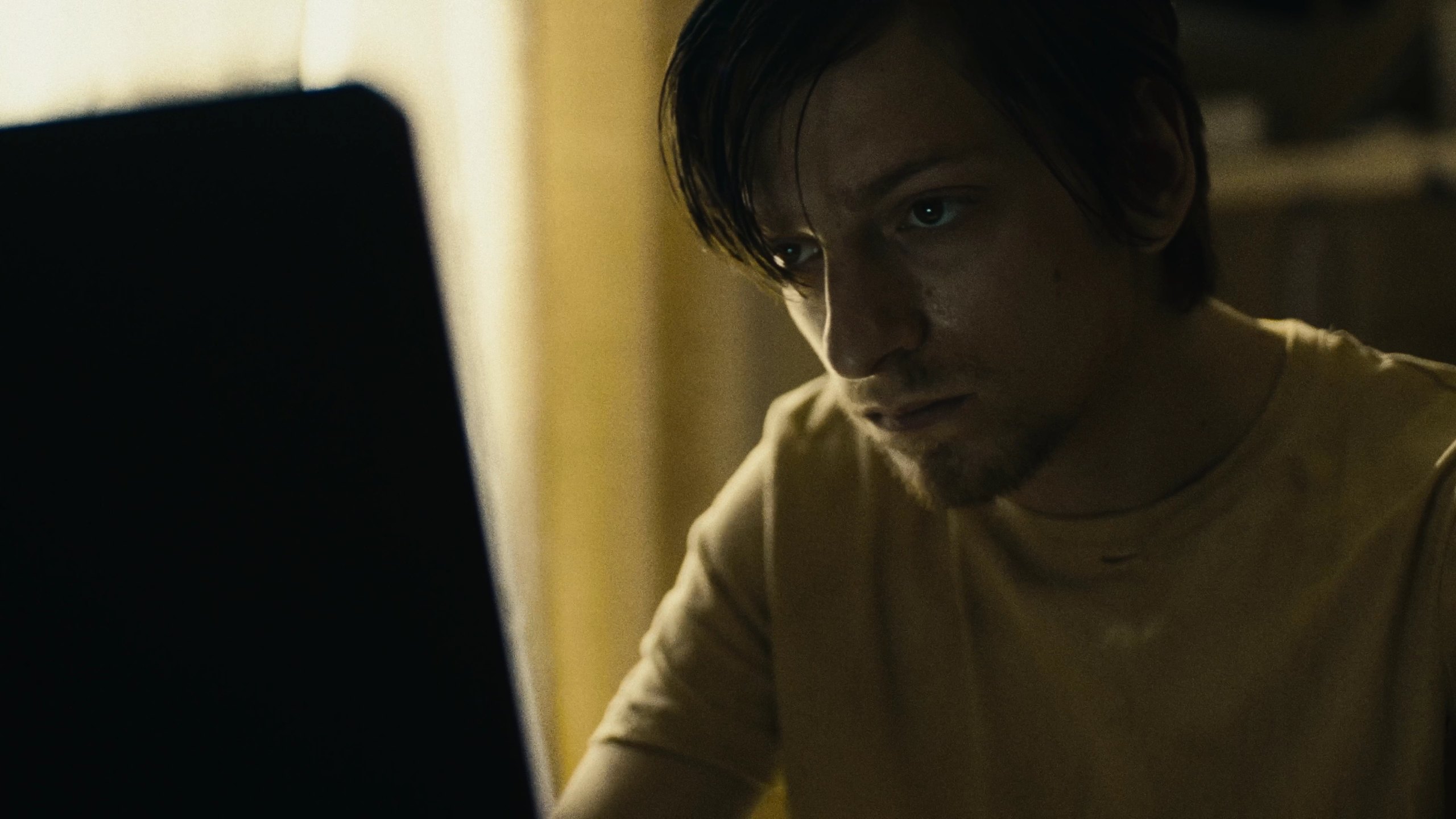 Close-up of a man with dark hair lit by a screen, looking intently ahead.