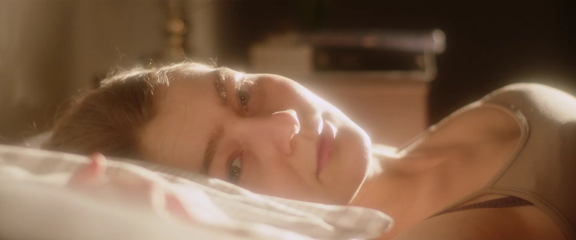 A woman lies on a pillow in warm backlight, looking toward the camera.